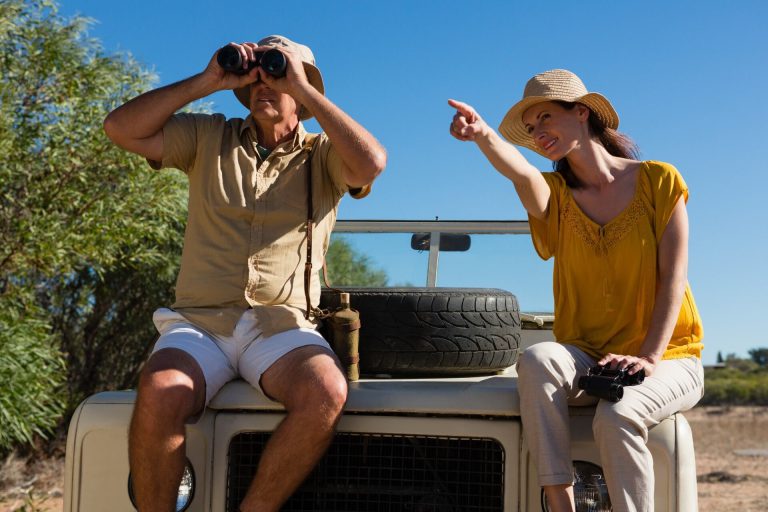 Two travellers with binoculars on the roof of a safari vehicle